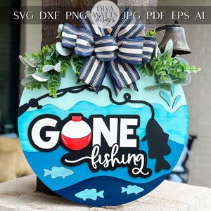 May include: A blue and white wooden sign with the words "Gone Fishing" in black lettering. The sign is decorated with a blue and white striped bow, green leaves, and a fishing lure.