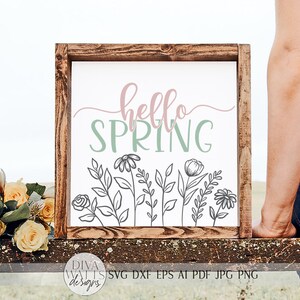 May include: A wooden sign with the text "hello spring" in pink and green lettering. The sign is decorated with a row of black line drawings of flowers and leaves.