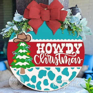 以下が含まれることがあります： 赤いリボン、緑、そして「HOWDY Christmas」の文字が入った、丸い木製のクリスマスドアハンガー。 デザインには、カウボーイハット、クリスマスツリー、牛柄が含まれています。