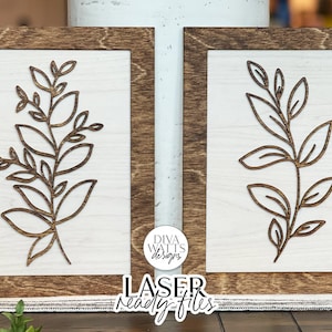 May include: Two wooden signs with a brown frame and a white background. Each sign features a laser-cut design of a leafy branch with a simple, minimalist style. The signs are labeled "LASER ready-to-files" and "DIVA WATTS Designs".