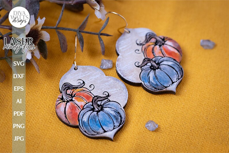 May include: A pair of silver-toned earrings with a pumpkin design. The pumpkins are painted in shades of orange, blue, and green. The earrings are hanging from gold-toned hooks.