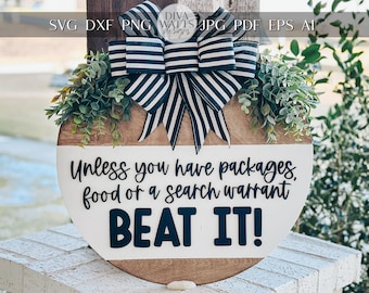 Könnte beinhalten: Ein rundes Holzschild mit weißem Hintergrund und schwarzem Text, der "Unless you have packages, food or a search warrant BEAT IT!" lautet. Das Schild ist mit einer schwarz-weißen Schleife und grünem Laub verziert.