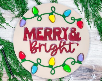 May include: A round wooden sign with the words "Merry & Bright" in red lettering. The sign is decorated with a string of colorful lights.