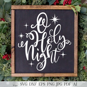 May include: A black framed sign with a white inscription that reads "O Holy Night" with stars around the text. The sign is surrounded by green foliage with red berries.