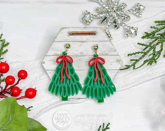 May include: Green Christmas tree earrings with red bow accents. The earrings are displayed on a wooden hexagon-shaped stand, surrounded by holiday greenery and berries. The earrings have gold-colored posts.