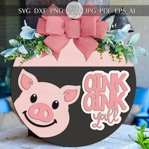 May include: A round wooden sign with a pink and black design, featuring a pig face and the words "OINK OINK y'all". The sign is decorated with a pink bow and greenery. The sign is a decorative item.