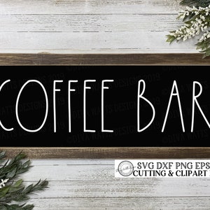 Puede incluir: Un letrero de pizarra negra con texto blanco que dice "COFFEE BAR". El letrero está enmarcado en un marco de madera marrón y está colgado en una pared de madera blanca. El letrero está rodeado de plantas verdes y flores blancas.