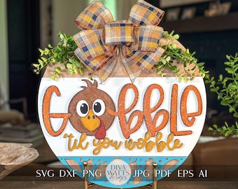 May include: A round wooden sign with a blue and white patterned border. The sign features a turkey illustration and the text "Gobble 'til you wobble". The sign is decorated with a plaid bow and greenery.