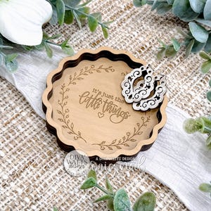 May include: A wooden tray with a scalloped edge and a dark brown rim. The tray has the phrase "It's just the little things" engraved inside a floral wreath. Two decorative earrings are placed on the tray.