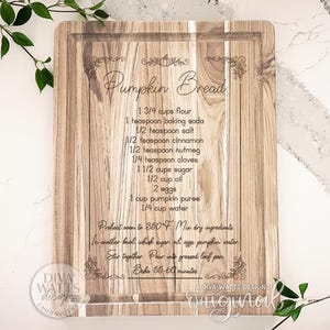 May include: Wooden cutting board with a carved recipe for pumpkin bread. The recipe includes ingredients like flour, baking soda, and pumpkin puree. The board has a rectangular shape with a groove around the edge.