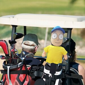 May include: A blue and white golf cart with two people and golf clubs. The cart has a red, black, and white golf bag in the back. The person in the front is wearing a blue hat and a yellow shirt. The person in the back is wearing a black shirt.