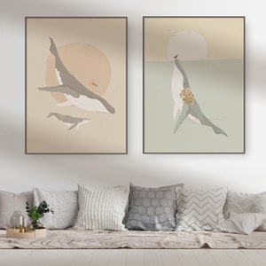 May include: Two framed prints of whale illustrations. The first print features a whale with a smaller whale swimming below it, against a light brown background with a sun. The second print features a whale with a bouquet of flowers, against a light green background with a sun.