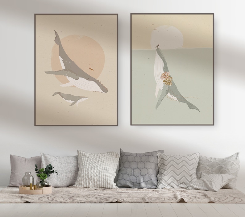 May include: Two framed prints of whale illustrations. The first print features a whale with a smaller whale swimming below it, against a light brown background with a sun. The second print features a whale with a bouquet of flowers, against a light green background with a sun.