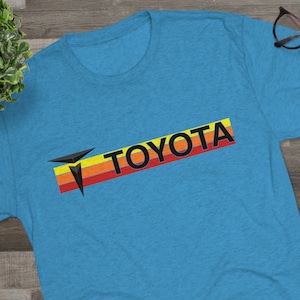 May include: A blue t-shirt with a retro-style Toyota logo in black, red, orange, and yellow.