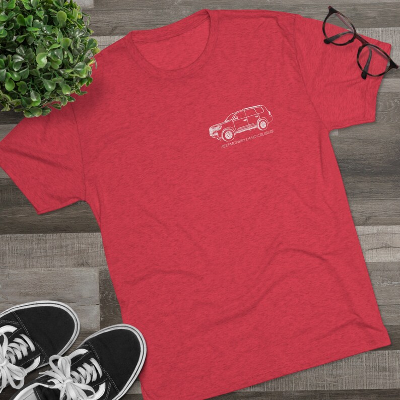 K&ouml;nnte beinhalten: Rotes melierter T-Shirt mit einer wei&szlig;en Umrandung eines Toyota Land Cruiser. Der Text "REMARKABLY LAND CRUISER" ist unter dem Fahrzeug aufgedruckt.