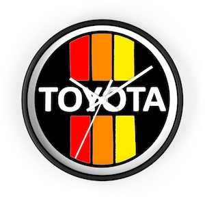 Puede incluir: Un reloj de pared negro y blanco con un diseño a rayas rojo, naranja y amarillo y la palabra "TOYOTA" en letras blancas.