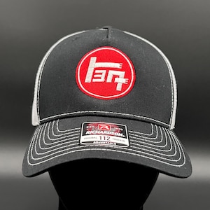 May include: Black and white trucker hat with a red circle and white logo that says "137". The hat is made by Richardson and is adjustable.