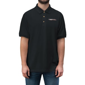 May include: Black polo shirt with a small embroidered logo that says "TRD Off Road" in white and red lettering.