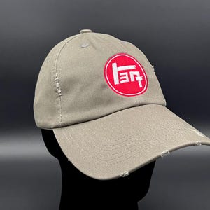 Puede incluir: Una gorra de béisbol gris desgastada con un círculo rojo y un logotipo blanco que dice "トヨタ".
