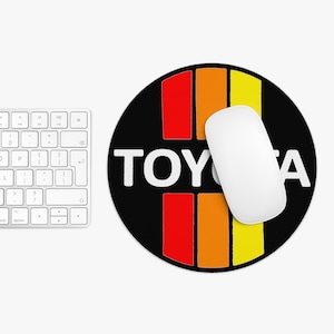 Könnte beinhalten: Eine runde schwarze Mausmatte mit einem weißen "TOYOTA"-Logo und einem rot-orange-gelben Streifenmuster.