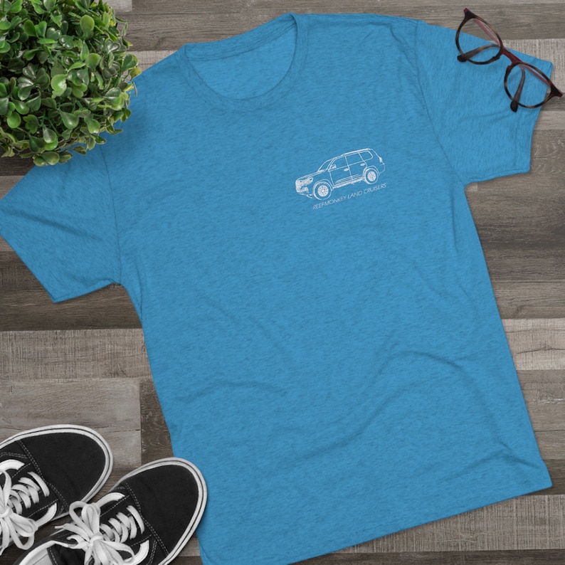 K&ouml;nnte beinhalten: Ein blaues T-Shirt mit einer wei&szlig;en Umrandung eines Toyota Land Cruiser auf der Vorderseite. Der Text "Legendary Land Cruiser" ist unter dem Auto aufgedruckt.