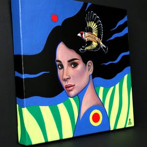 May include: A square canvas painting featuring a portrait of a person with long black hair flowing against a blue and black background. A small goldfinch flies above the head. The lower section displays green and yellow stripes with a red circle.