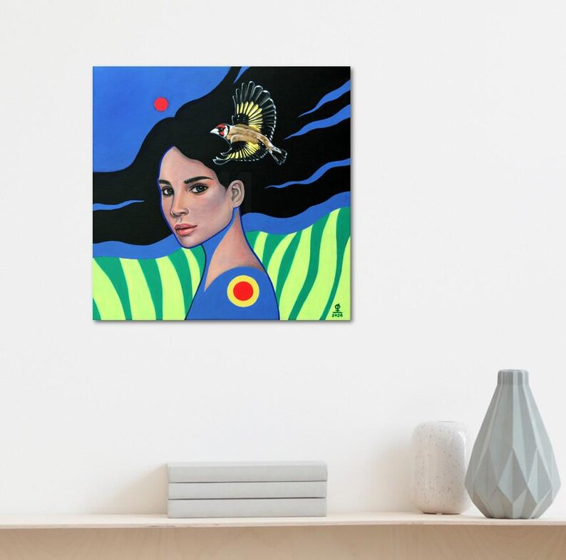 May include: A square painting featuring a portrait of a person with long black hair flowing into a dark background. A small bird with yellow and black wings is perched above the head. The lower section displays green vertical stripes and a blue shirt.