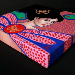 May include: A square canvas painting featuring a stylized portrait of a person with dark hair, accented by a gold butterfly motif. The composition incorporates vibrant pink, blue, and green geometric patterns with red polka dots and a central red circle.