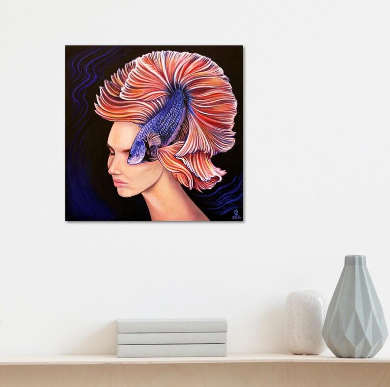 May include: A square canvas painting depicting a profile view of a person with a large, vibrant orange and pink betta fish tail flowing from their head like hair. The fish body is purple and blue, set against a dark background with blue wavy lines.