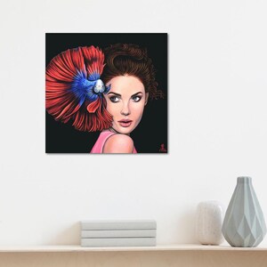 May include: A square wall art print featuring a digital illustration of a person with brown hair looking over their shoulder. A vibrant red and blue betta fish is positioned behind the person's head, with its large, flowing fins fanned out.