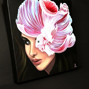 May include: A square canvas painting on a black background featuring a portrait of a person with dark hair. A large, white and pink betta fish with flowing fins is positioned over the upper portion of the face, partially obscuring one eye.