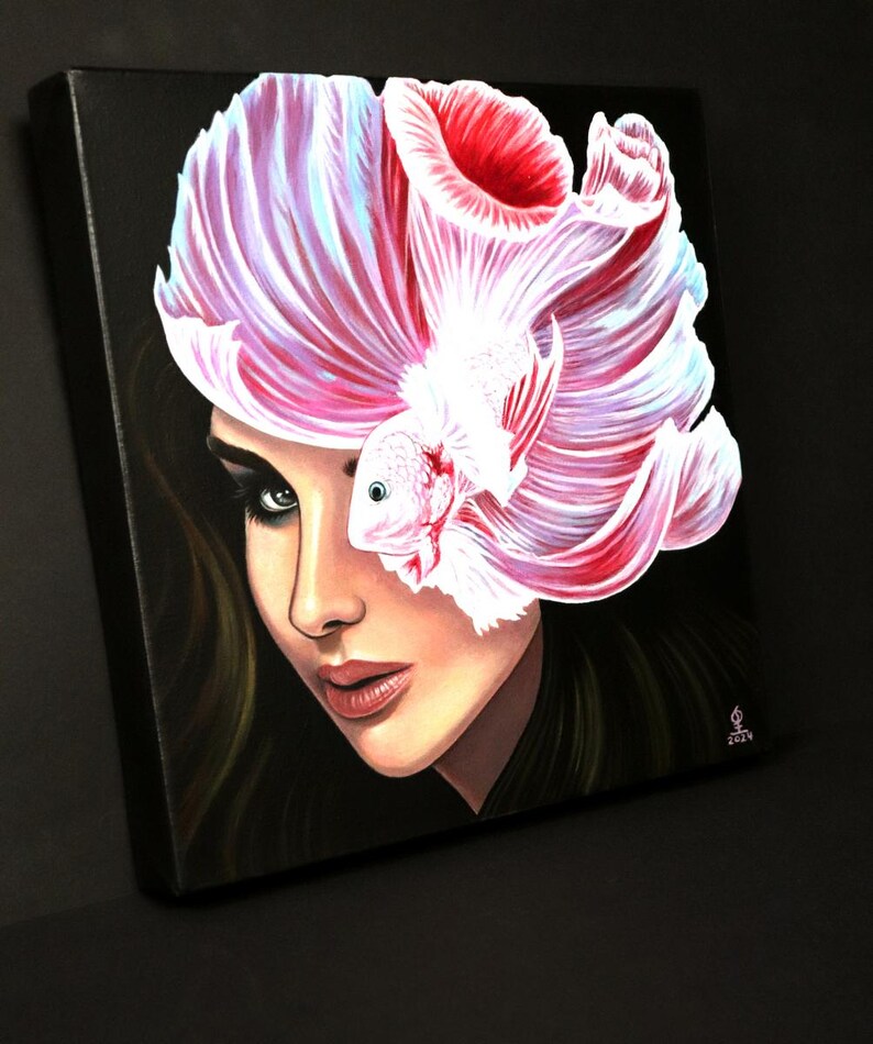 May include: A square canvas painting on a black background featuring a portrait of a person with dark hair. A large, white and pink betta fish with flowing fins is positioned over the upper portion of the face, partially obscuring one eye.