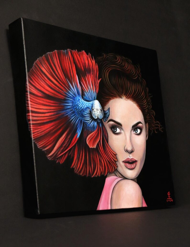 May include: A square canvas painting on a black background featuring a portrait of a person with brown hair and a pink top, positioned next to a large, vibrant betta fish with flowing red and blue fins that frame the side of the person's face.