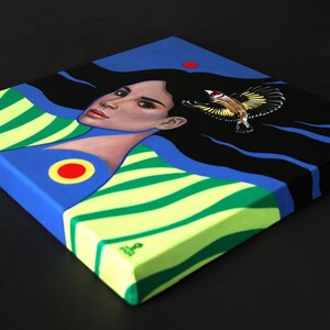 May include: A square canvas painting featuring a person with long black hair flowing across a dark blue background. The person wears a lime green and dark green striped garment with a red and yellow circular emblem. A small bird is in flight.