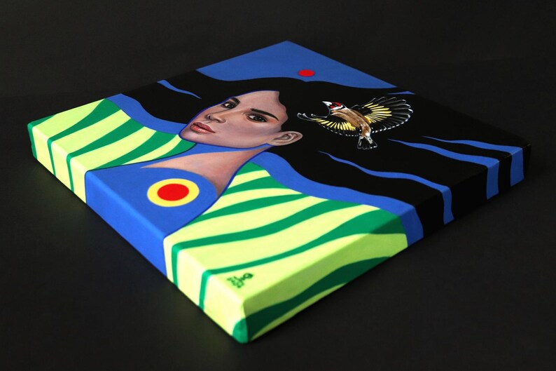 May include: A square canvas painting featuring a person with long black hair flowing across a dark blue background. The person wears a lime green and dark green striped garment with a red and yellow circular emblem. A small bird is in flight.