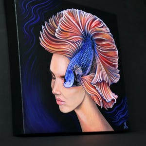 May include: A square canvas painting on a black background featuring a profile view of a person with a blue betta fish replacing their hair. The fish has long, flowing orange and red fins that fan out behind the head, and the painting includes blue wavy lines.