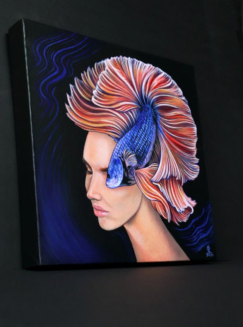 May include: A square canvas painting on a black background featuring a profile view of a person with a blue betta fish replacing their hair. The fish has long, flowing orange and red fins that fan out behind the head, and the painting includes blue wavy lines.