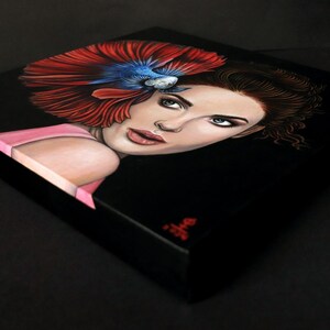 May include: A square canvas painting on a black background featuring a portrait of a person with brown hair. A vibrant red and blue betta fish is positioned above the person's head, with its flowing fins fanning out across the upper left side.
