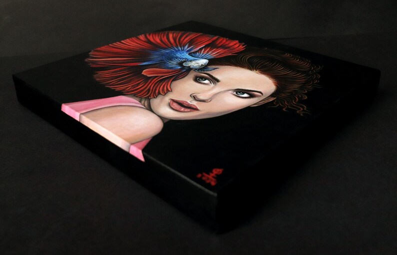 May include: A square canvas painting on a black background featuring a portrait of a person with brown hair. A vibrant red and blue betta fish is positioned above the person's head, with its flowing fins fanning out across the upper left side.
