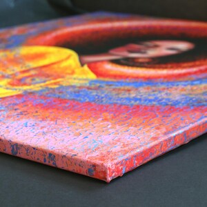 May include: An abstract painting on canvas featuring a woman's face. The artwork uses a vibrant color palette of red, orange, yellow, and blue. The canvas is stretched and mounted, showcasing the side profile of the artwork.