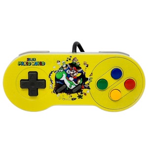 Può includere: Controller Super Nintendo giallo con un design di Super Mario World che mostra Mario che cavalca Yoshi. Il controller ha quattro pulsanti colorati: blu, verde, giallo e rosso.