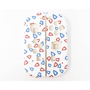May include: White Nintendo Switch Joy-Con controllers with a pattern of red and blue triangles. The controllers have white buttons and directional pads. The design is a playful and colorful accessory for the gaming console.