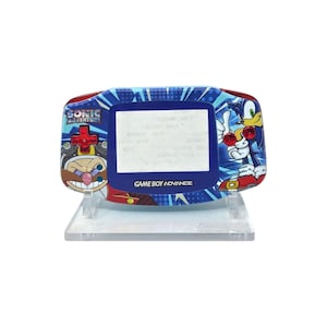 May include: A blue Game Boy Advance console with Sonic the Hedgehog and Dr. Eggman illustrations. The console has a blue screen and the text "SONIC ADVENTURE" and "GAME BOY ADVANCE" are displayed.