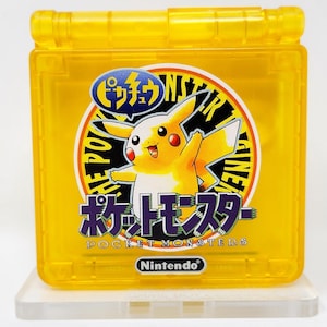 Może przedstawiać: Żółta przenośna konsola do gier Game Boy Color z postacią Pikachu z przodu. Konsola ma okrągły wzór w kolorze czarno-białym z tekstem "The Power of the Pokemon Engine" i "Pocket Monsters" w języku japońskim i angielskim. Konsola stoi na białym stojaku.