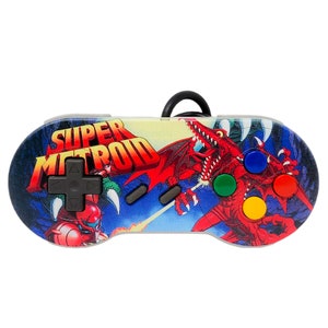 May include: A Super Metroid themed Super Nintendo controller with a red dragon and a blue and green space suit character on the front. The controller has four buttons, a directional pad, and two shoulder buttons.