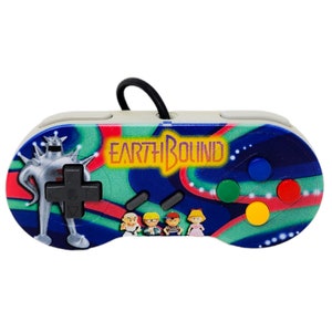 May include: A white Super Nintendo controller with a blue, green, and pink design. The controller features the text "EARTHBOUND" and characters from the game.