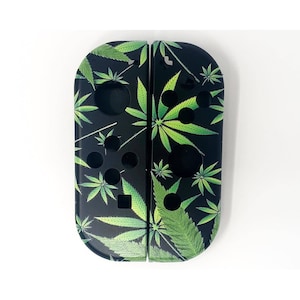 Puede incluir: Un par de mandos Joy-Con negros para Nintendo Switch con un patrón de hojas de marihuana verdes.
