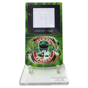 May include: A green Game Boy Color handheld game console with a Power Rangers design. The console features a black screen, buttons, and the text "GAME BOY COLOR". The Power Rangers logo and a green ranger are displayed on the front.