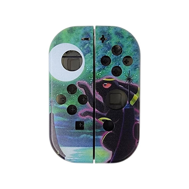May include: A green, blue, and black Nintendo Switch Joy-Con controller skin featuring a Pokemon character. The character is a black creature with a yellow star on its forehead. The background is a starry night sky with a white moon.