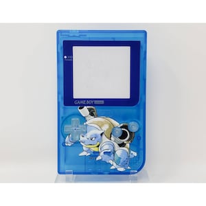 May include: A blue Game Boy Pocket handheld video game console with a Blastoise character graphic on the front. The console has a blue screen and a white power button.